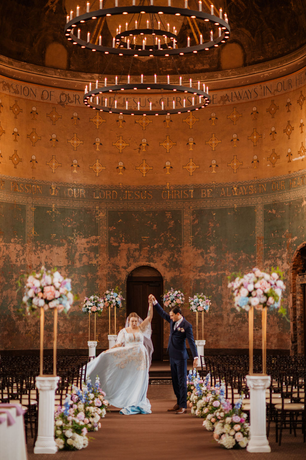 Bride and groom dancing at altar of ornate historic chapel with pastel faux floral aisle columns in pink, blue, and white, The Monastery wedding venue Cincinnati Ohio