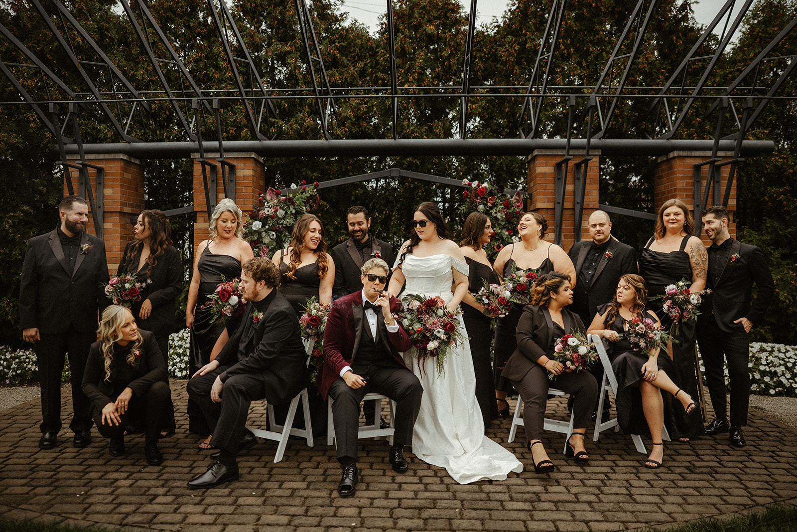 Wedding party in all black attire with burgundy, blush, and white faux bouquets in front of lush faux floral ceremony arch, Steam Plant wedding Dayton Ohio
