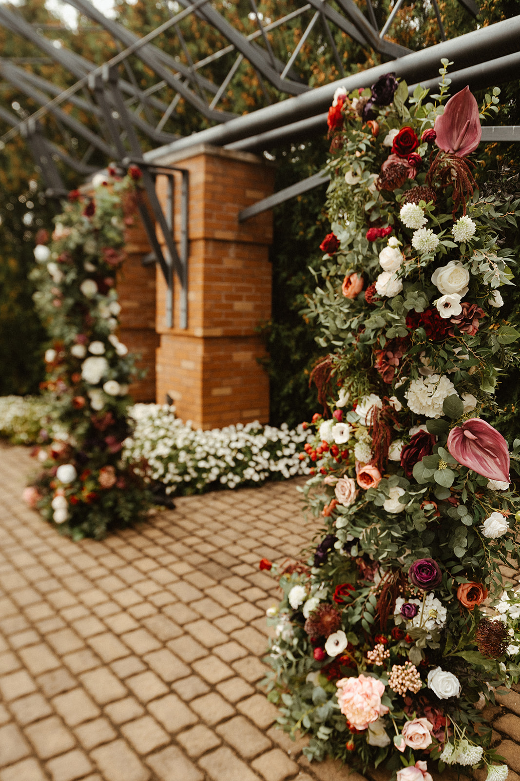 Close-up of lush faux floral ceremony arch with burgundy roses, anthurium, white hydrangea, and greenery, Steam Plant outdoor fall wedding Dayton Ohio