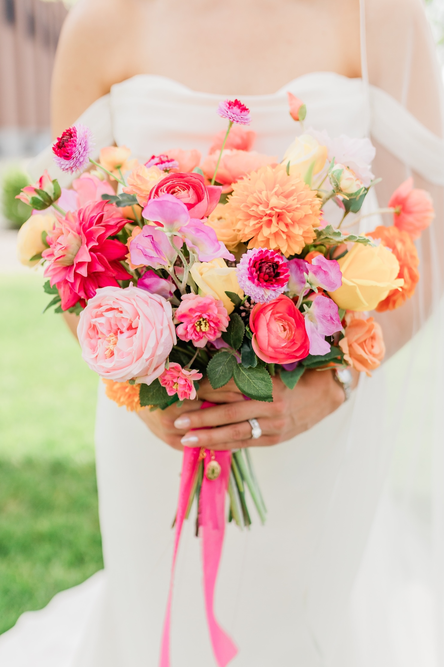 Vibrant faux bridal bouquet with hot pink, coral, orange, and yellow silk roses, dahlias, and ranunculus with pink ribbon wrap